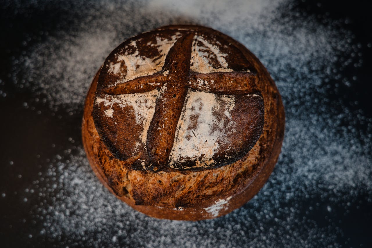 gallery-06 Freshly baked artisan bread with a rustic cross pattern, captured in a bakery setting.