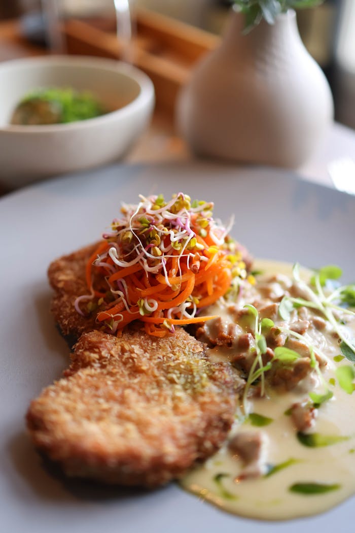 Delicious vegetarian schnitzel topped with fresh carrots and sprouts, and a creamy sauce, perfect for an elegant dining experience.