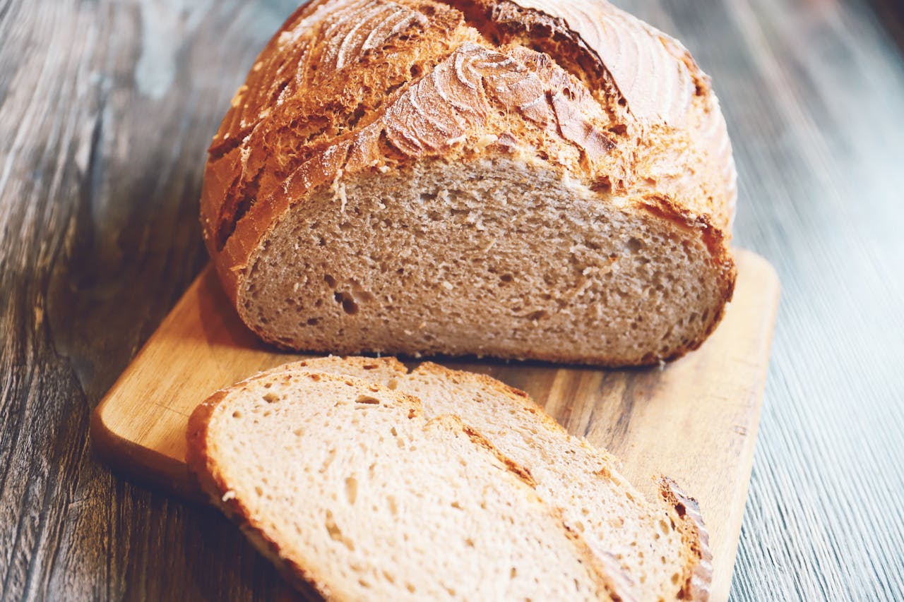 portfolio-02 Freshly baked rustic whole wheat bread loaf with slices on a wooden board.
